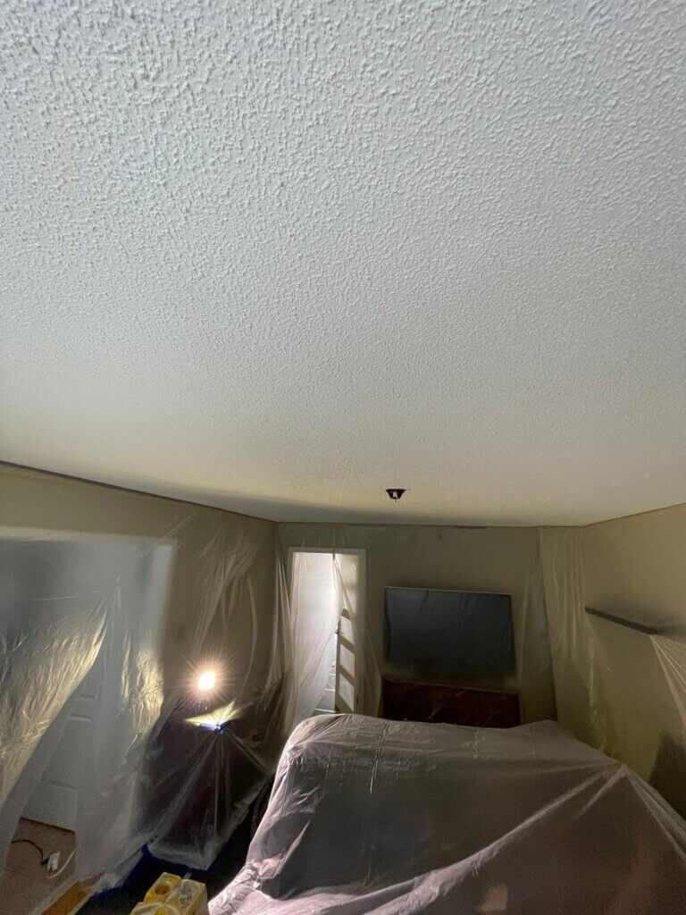 Interior of a room with furniture and walls covered in plastic before popcorn ceiling removal